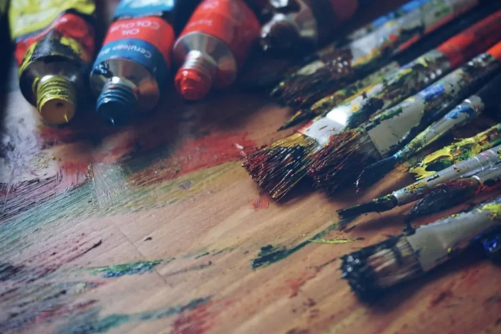 paint brushes covered in paint and paint tubes on a table