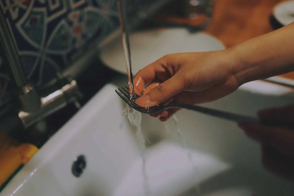 picture of hand washing a fork while water pours from a faucet