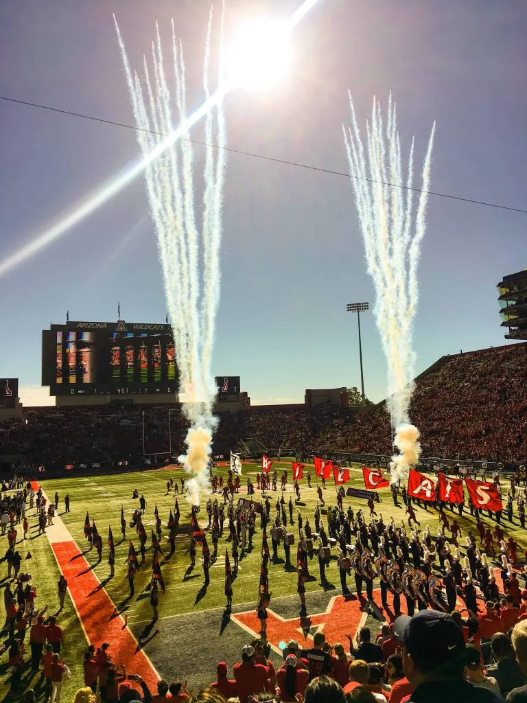 marching band on a football field with filled bleachers cheerleaders