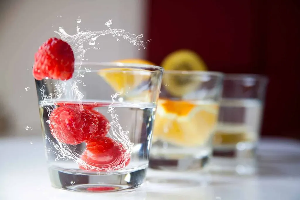 raspberries splashing into glass of water, lemon in glass of water, kiwi in glass of water