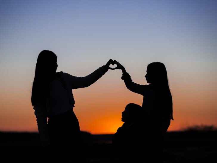 sunset with silhouette of adult woman and teen girl creating a heart with their hands