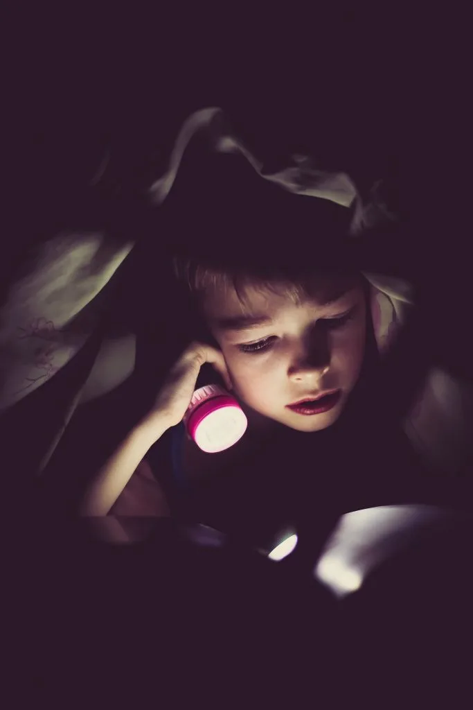 boy reading under covers with flashlight