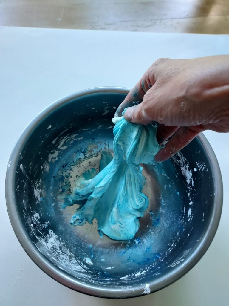 metal bowl with blue homemade slime being mixed by a hand