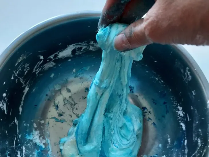 hand mixing homemade blue slime in metal bowl