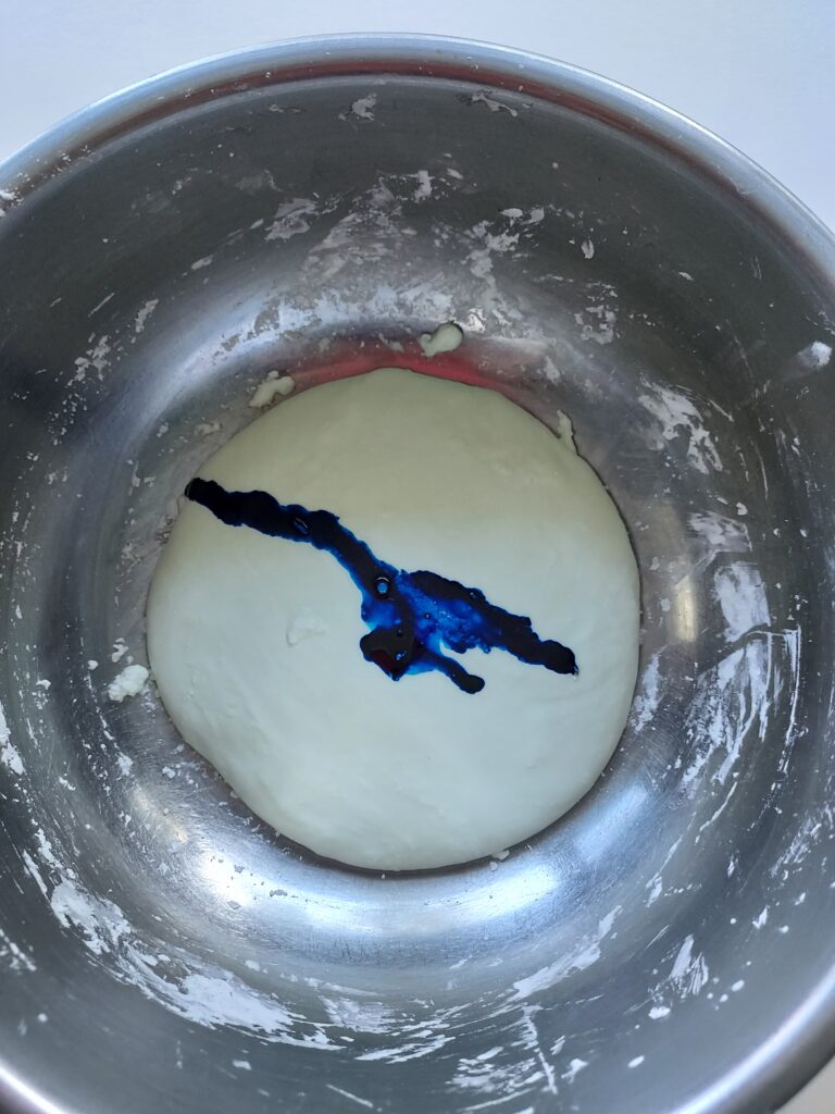 white homemade slime with drops of bright blue food coloring on top waiting to be mixed