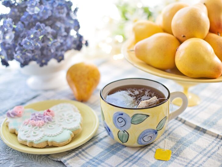 table setting with a full tea cup, butterfly shaped cookie, bowl of lemons and vase with lavender flowers