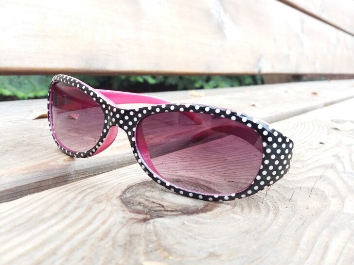 black oval sunglasses with white polka dots and hot pink on inner surfaces sitting on a table