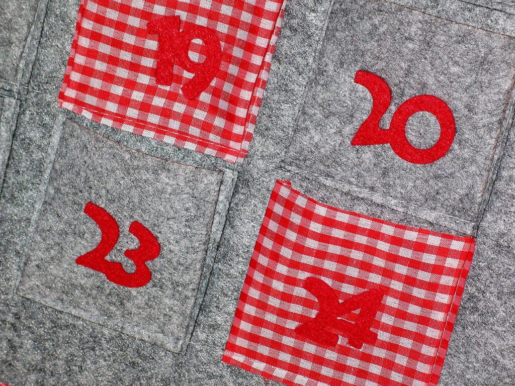 Gray felt pockets with numbers alternating with red and white checkered pockets numbered all on gray felt background for advent calendar