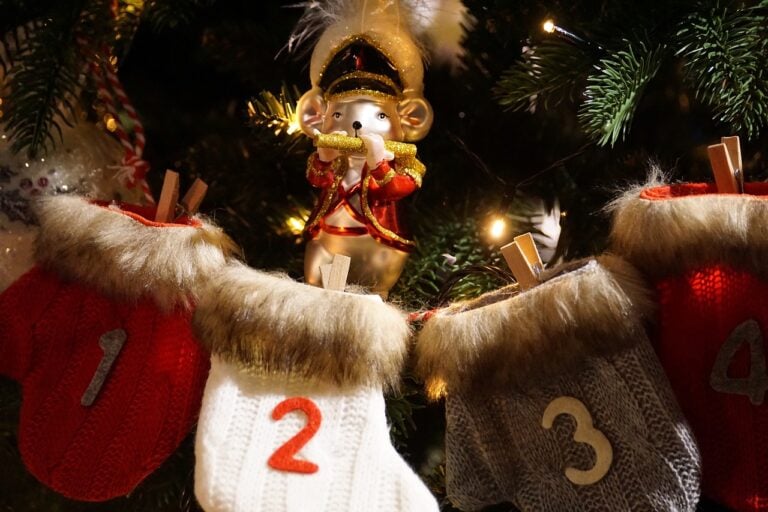 Christmas tree in background. knitted mittens in gray, white and red with numbers on them to use for advent calendar. Clipped to tree with clothespins
