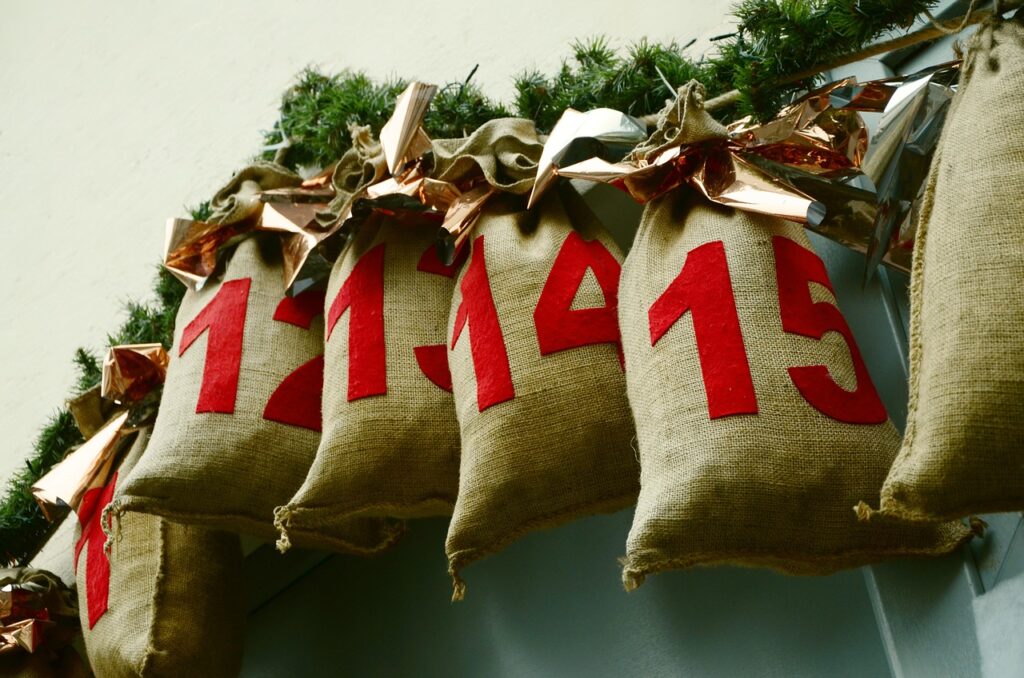fake pine bough gardland wrapped around rope. Burlap bags labeled with red numbers and tied to the rope with gold bows. Use for advent calendar