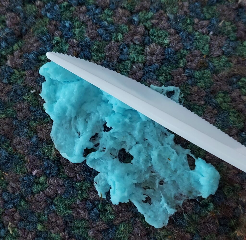 blue craft slime stuck to carpet being scraped with a knife