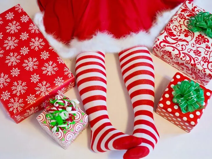 Elf dress or Mrs Santa dress hem showing with legs wearing red and white striped stockings, no shoes 4 gifts wrapped in red and white wrapping paper with green bows are next to the legs