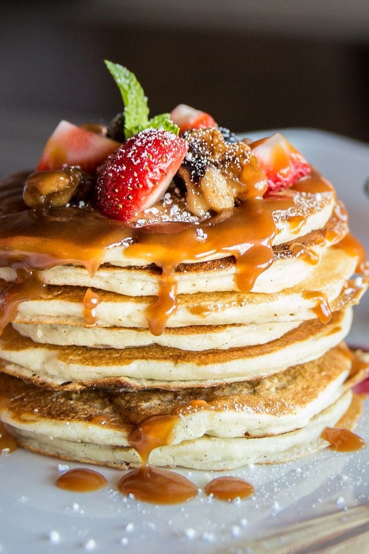stack of pancakes topped with fruit and caramel